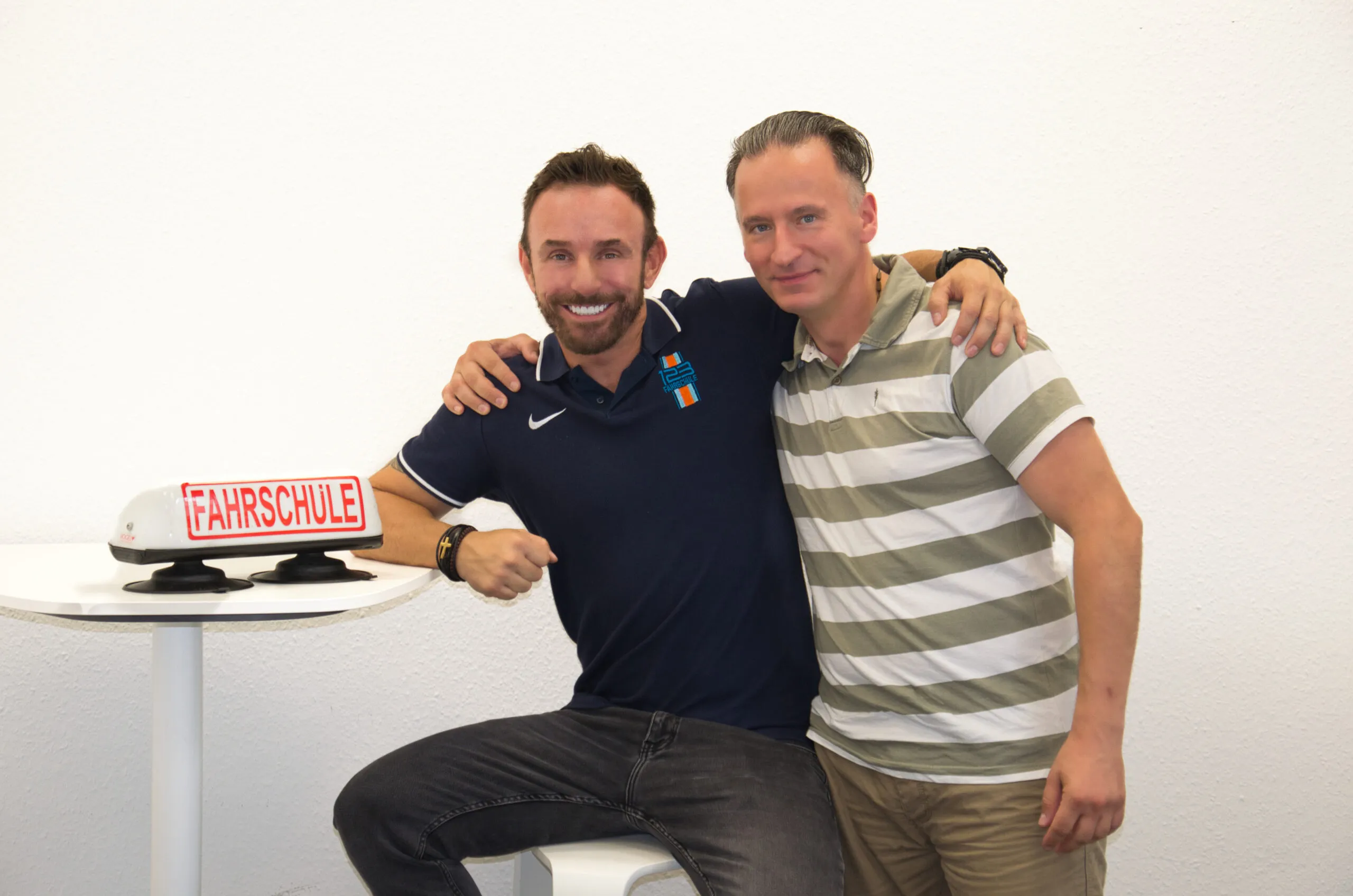 Fahrlehrer lehnt an Tisch mit einem Fahrschule-Dachschild.