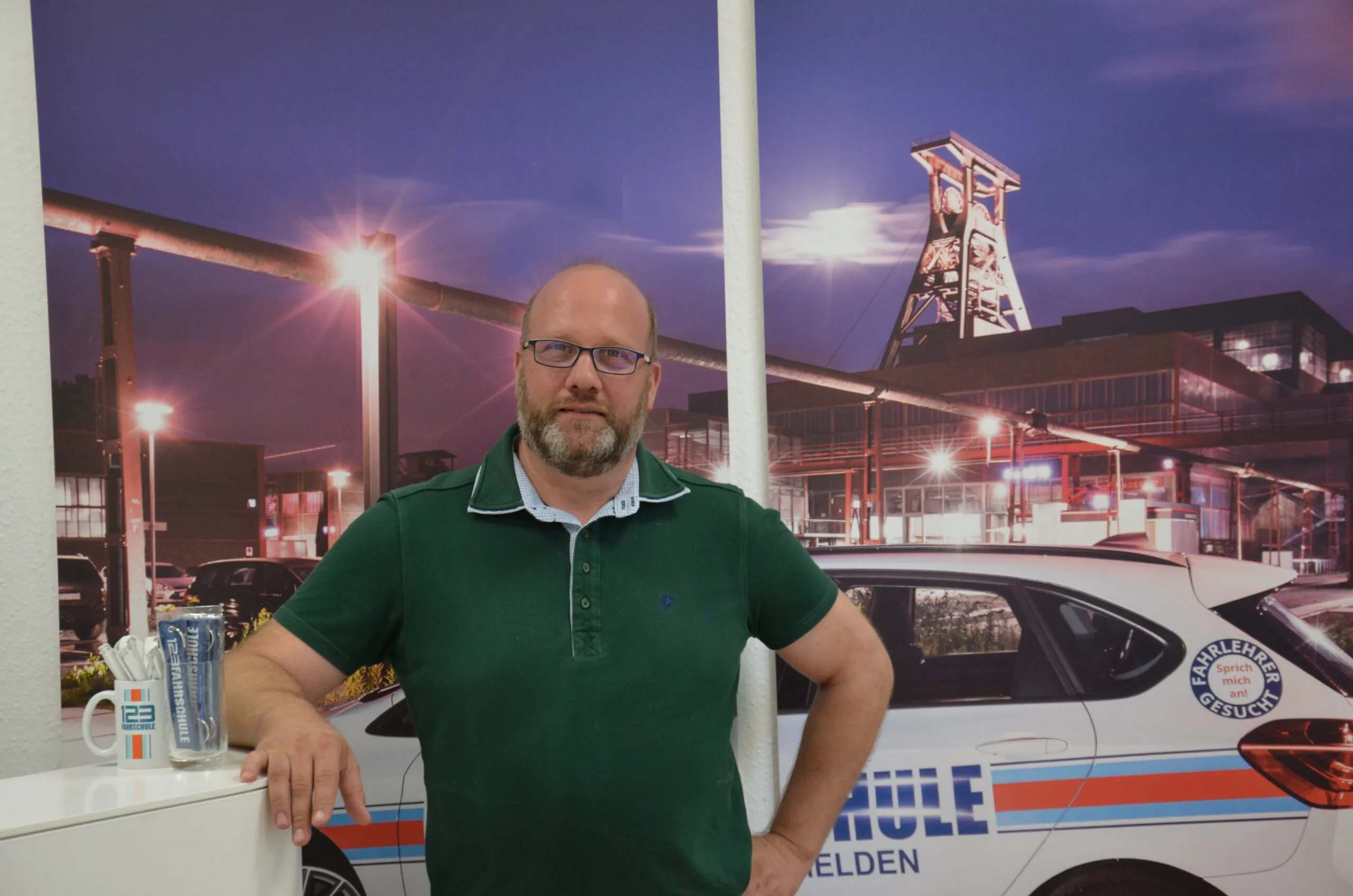Fahrlehrer steht vor Bild mit einem Fahrschule-Auto