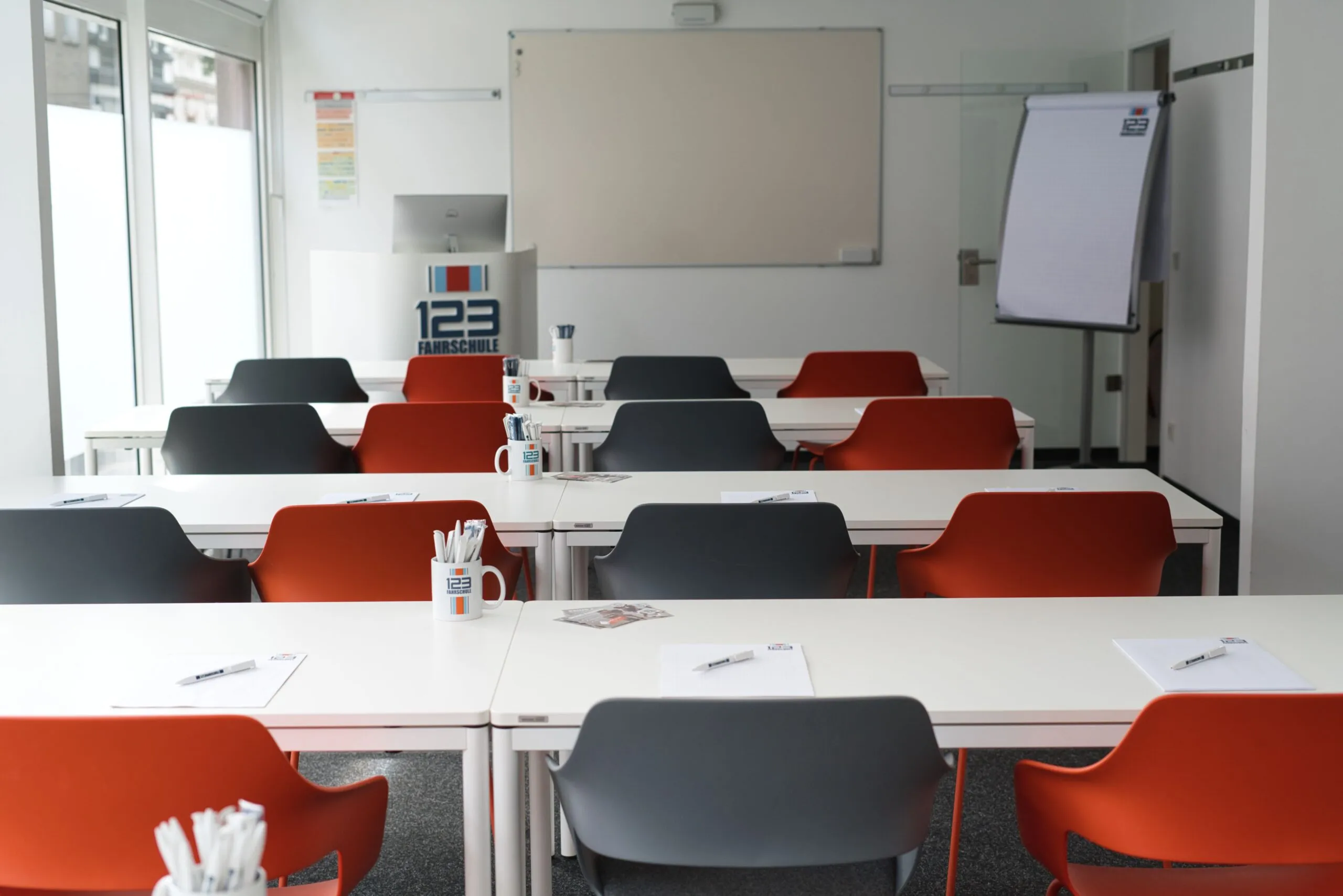 Raum für den Theorieunterricht der 123 Fahrschule-Filiale mit einer Lerntafel, Tischen und Stühlen
