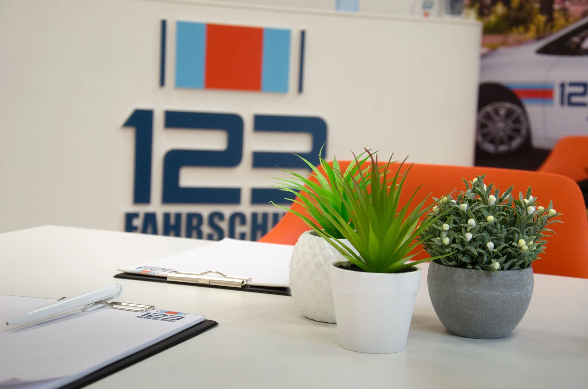Tisch einer Fahrschule mit grünen Pflanzen und Notizblöcken der 123 Fahrschule