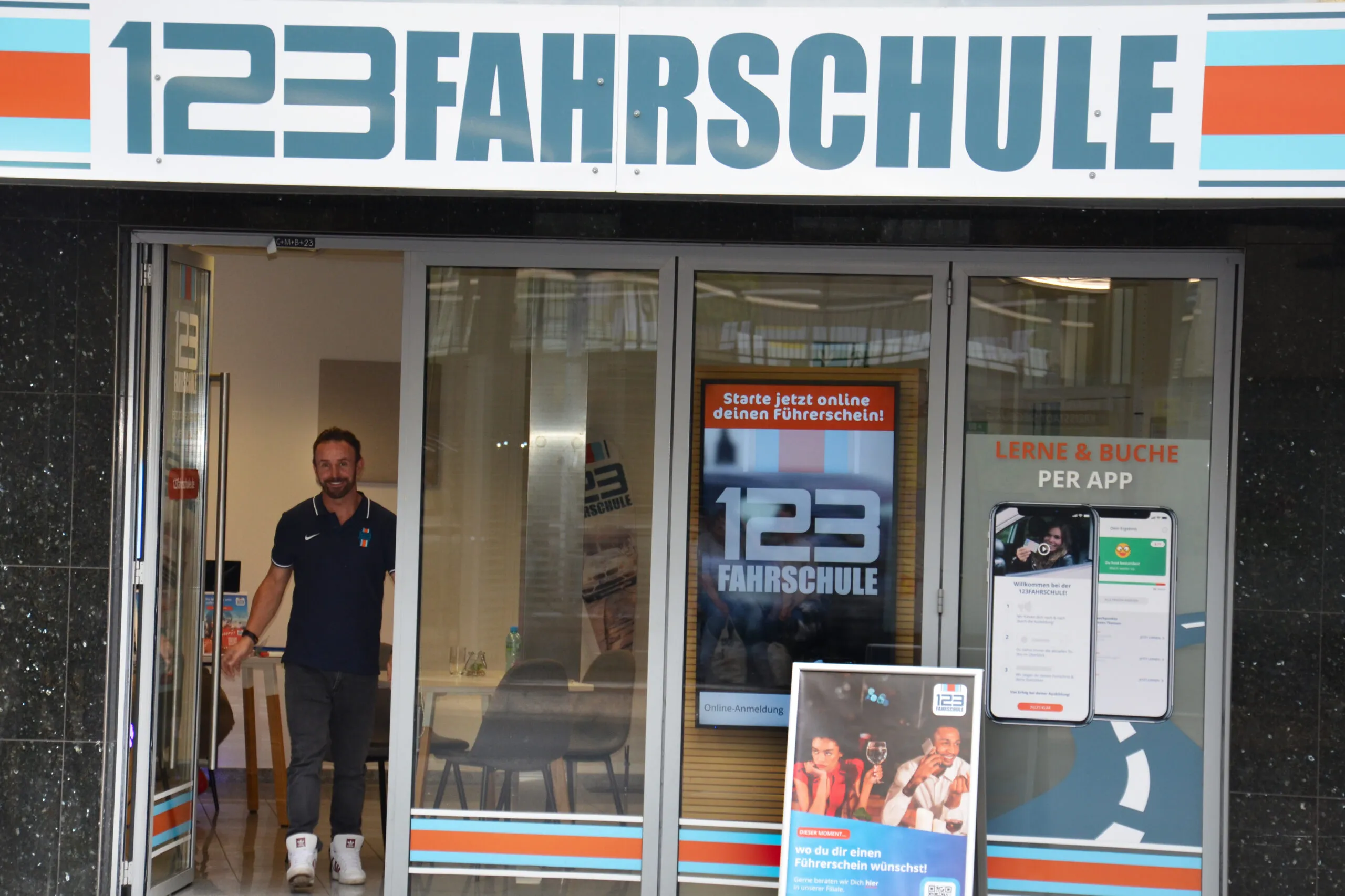 Ein Fahrlehrer der 123 Fahrschule steht an einer Tür der Filiale der 123 Fahrschule.